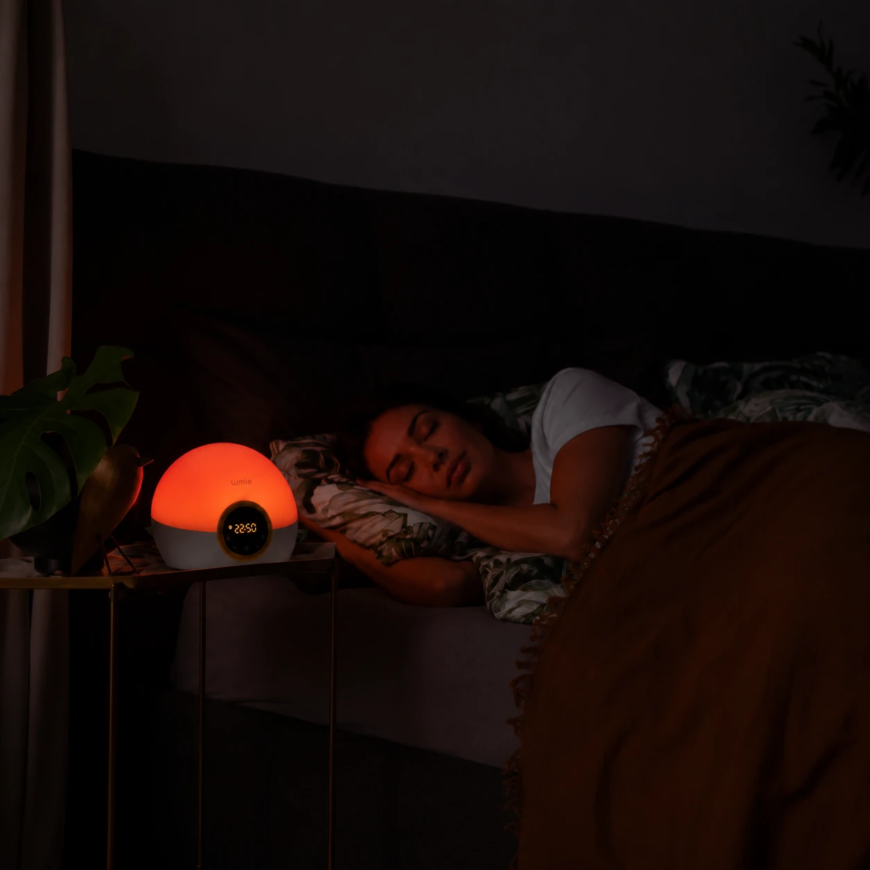 Lumie Bodyclock Rise100 alarm clock glowing red in a dark bedroom while a woman sleeps beside it. Lumie Bodyclock Rise100 alarm clock glowing red in a dark bedroom while a woman sleeps beside it.